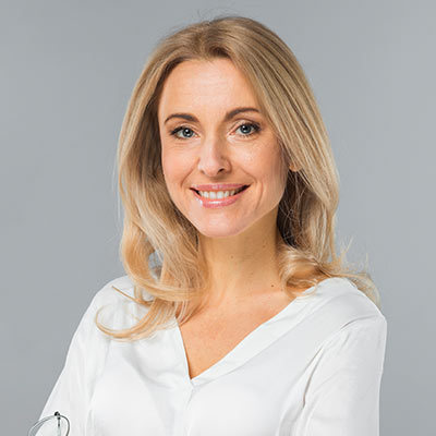 Portrait of a smiling blonde woman in a white blouse against a gray background.